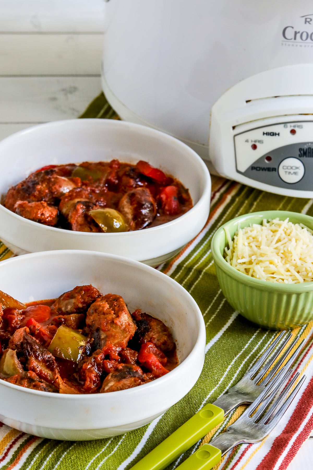 Slow Cooker Sausage and Peppers shown in two bowls with Parmesan and slow cooker in back.