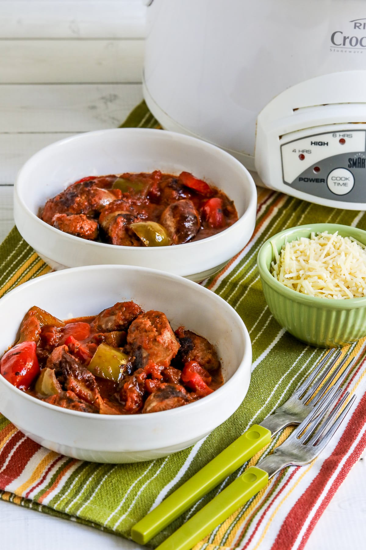 Slow Cooker Sausage and Peppers in two bowls with slow cooker and Parmesan in background.