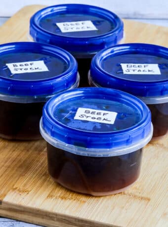 Square image showing beef stock in freezer containers on cutting board in freezer containers.