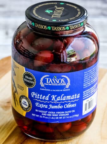 Square image of jar of Pitted Kalamata Olives on cutting board.