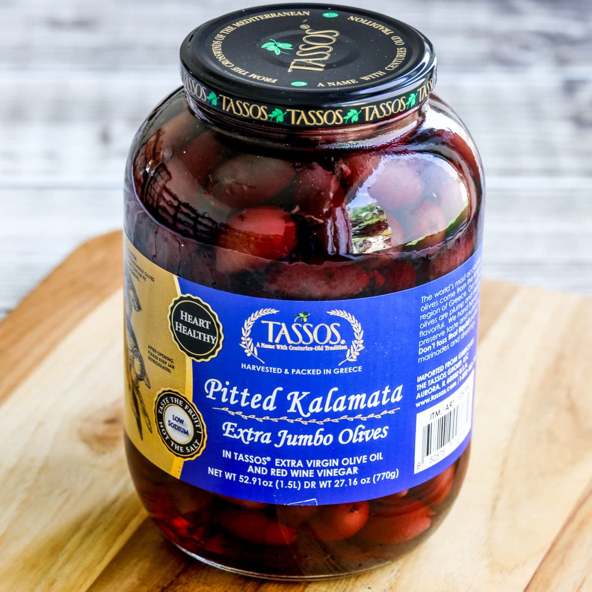 Square image of a jar of pitted Kalamata olives on a cutting board.