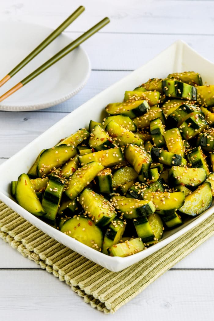 spicy cucumber salad in serving dish with plate and chopsticks in background