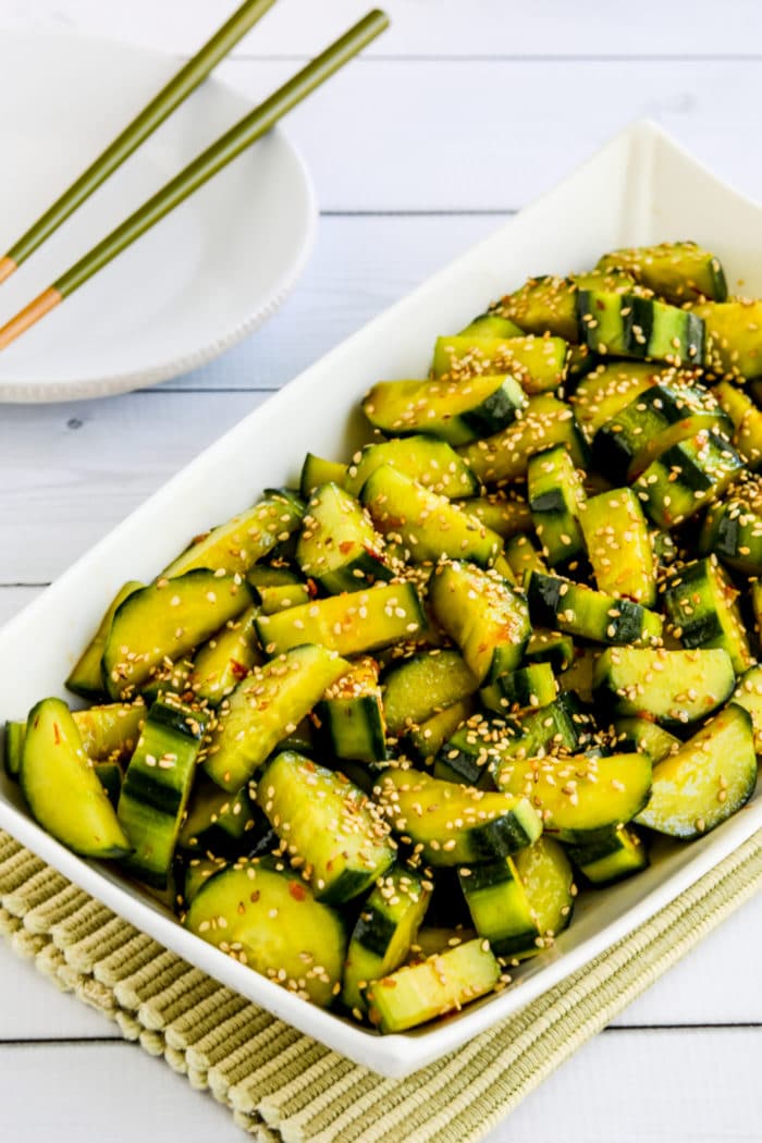 Spicy cucumber salad in serving dish with plate and chopsticks in background
