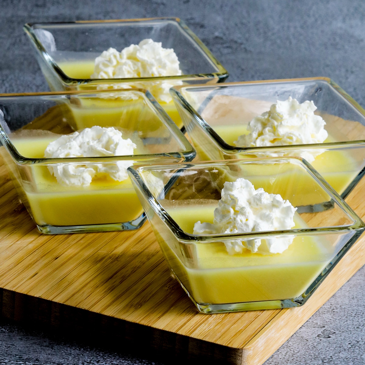 Square image for Sugar-Free Jelled Ricotta Pudding shown in four square dishes on cutting board, with whipped cream.