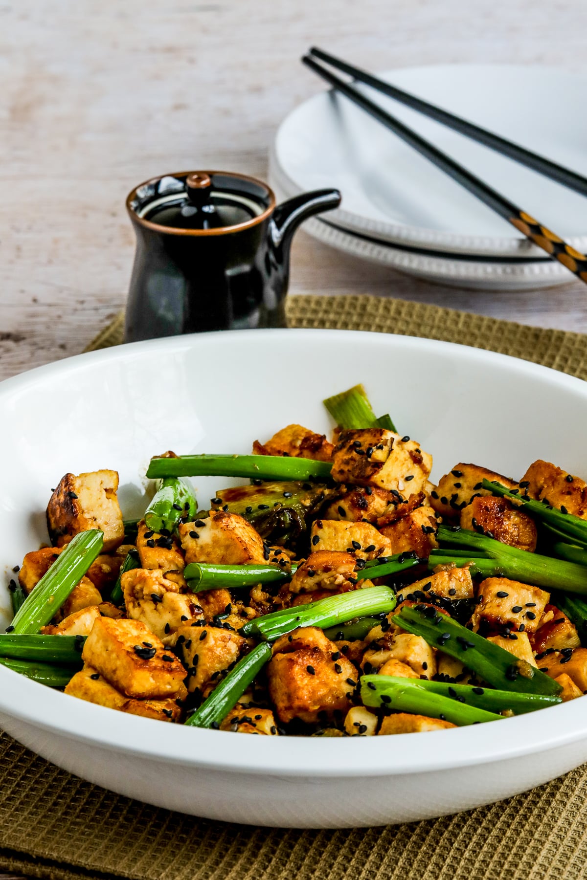 Stir-Fried Tofu with Ginger and Soy Sauce in serving dish with soy sauce and chopsticks on plate.
