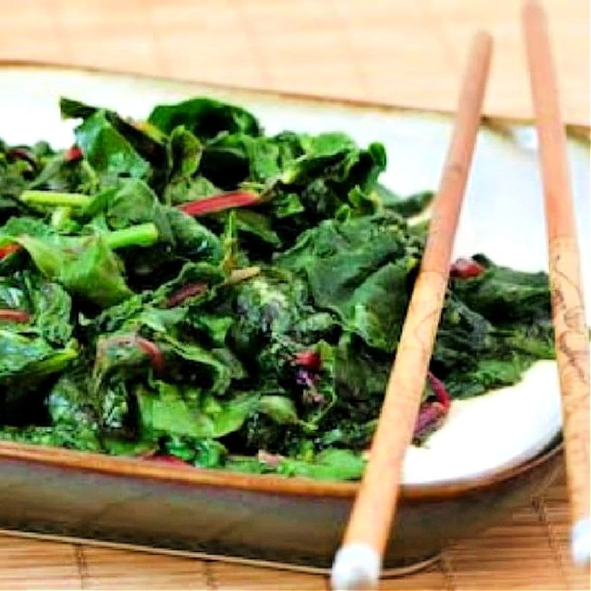 Square image of stir-fried radish greens on serving plate with chopsticks.