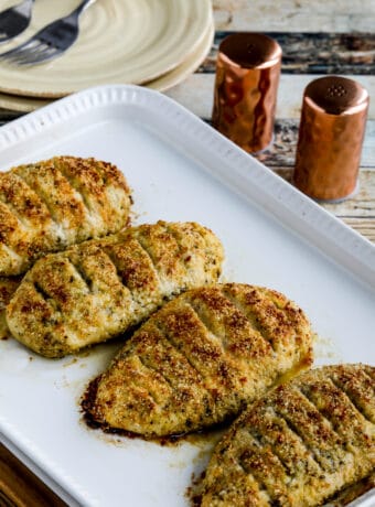 Baked Parmesan Crusted Chicken shown on serving platter with salt, pepper, and plates in background