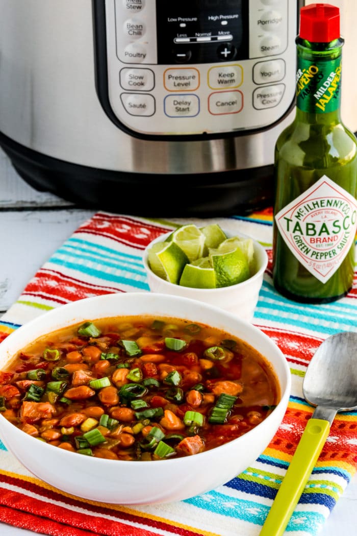 one serving of Instant Pot Ham and Bean Soup in bowl with limes, green Tobasco, and Instant Pot in background