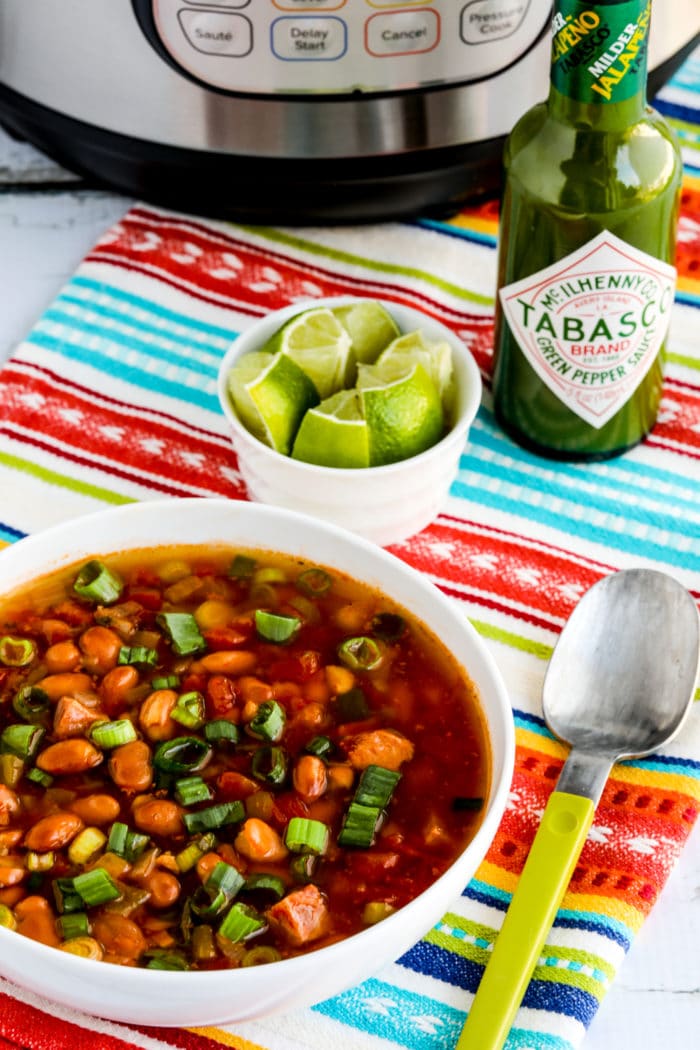 Instant Pot Ham and Bean Soup shown in serving bowl with limes, Green Tabasco, and Instant Pot in background