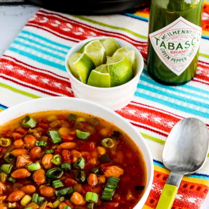 Instant Pot Ham and Bean Soup shown in serving bowl with limes, Green Tabasco, and Instant Pot in background