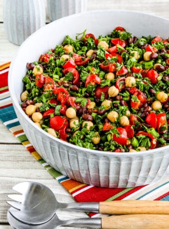 Balela Salad shown in serving bowl with serving spoons on striped napkin