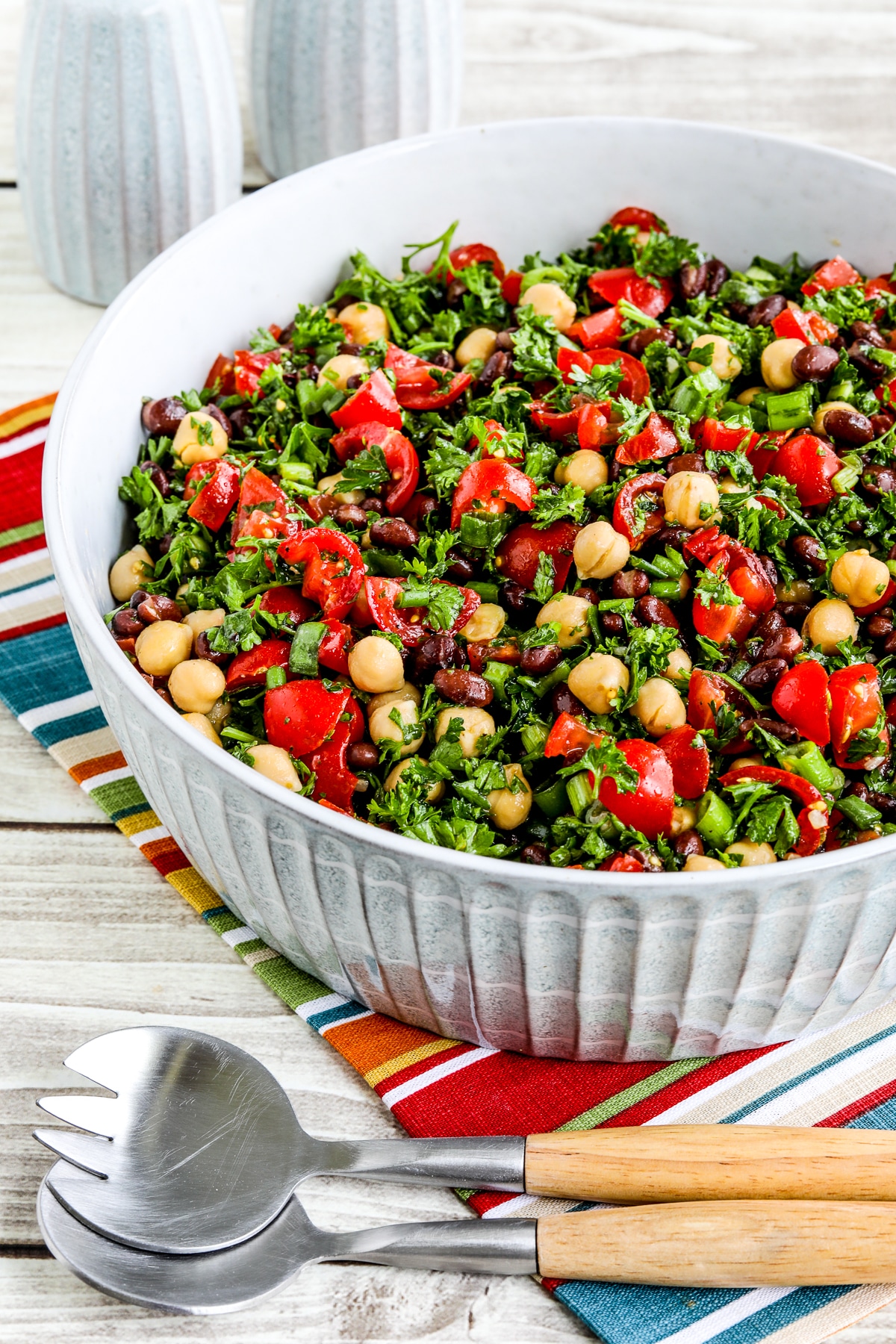 Balela Salad shown in serving bowl with serving spoons on striped napkin