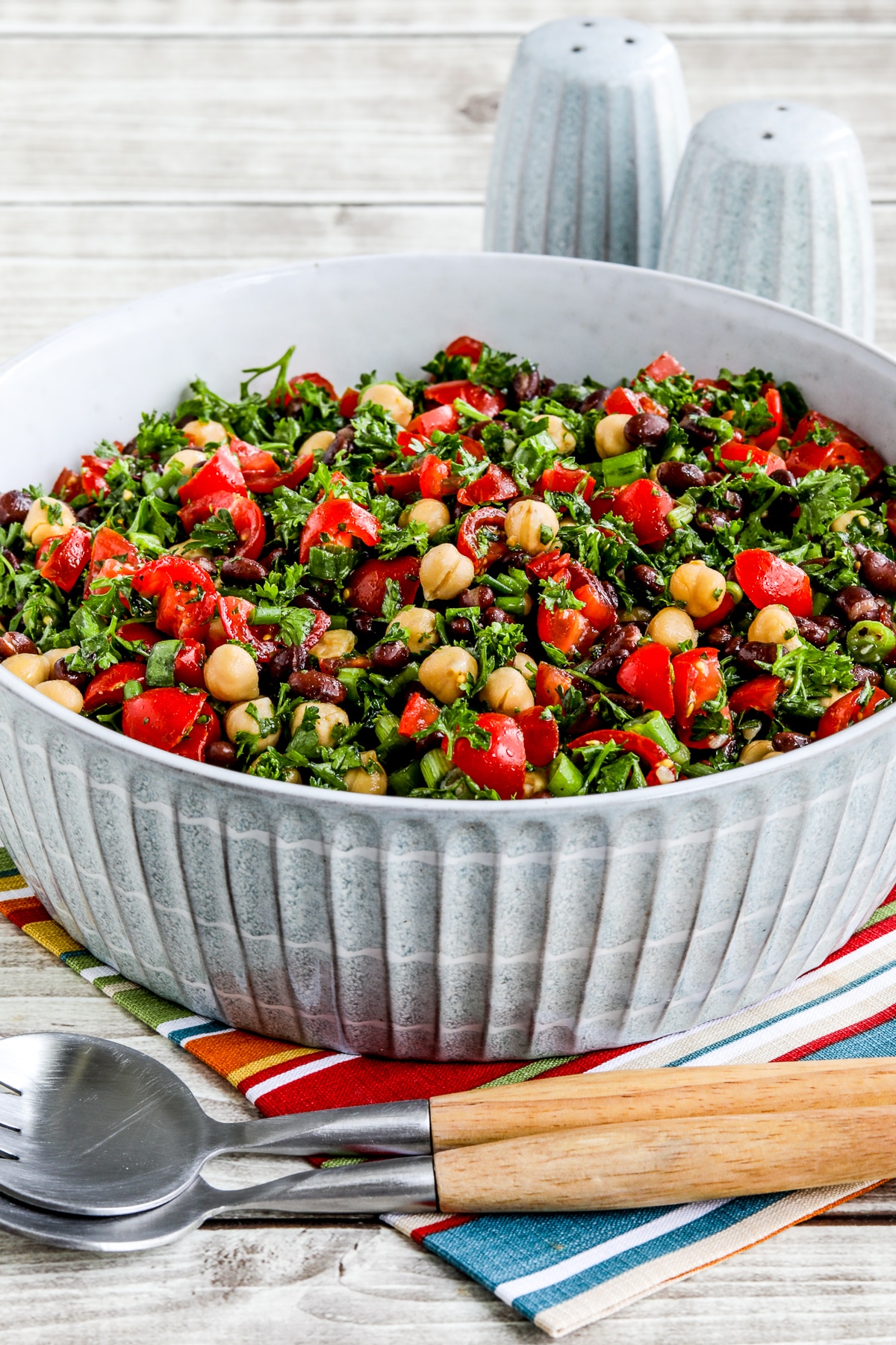 Balela Salad (Middle Eastern Bean Salad) in serving bowl with serving spoons, salt, pepper, and napkin