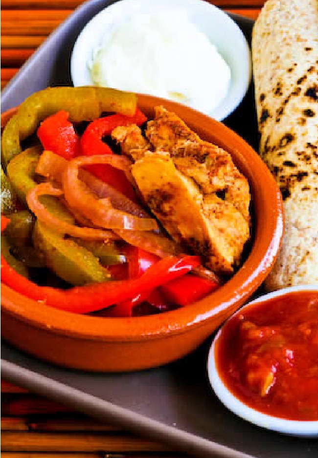 Slow cooker chicken fajitas on a square serving plate with low carb tortillas, sour cream and salsa.