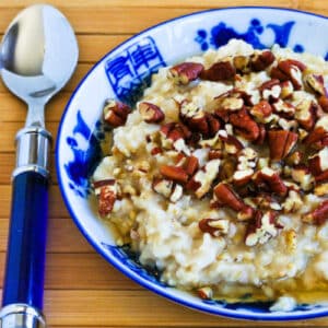 CrockPot Steel-Cut Oats shown in serving bowl with maple syrup and pecans.