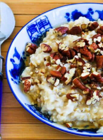 CrockPot Steel-Cut Oats shown in serving bowl with maple syrup and pecans.