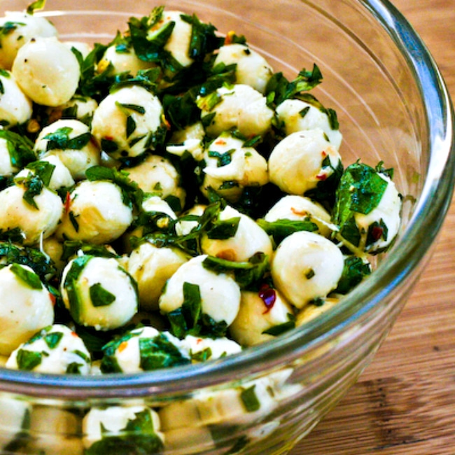 Marinated fresh mozzarella with chopped herbs shown in glass serving bowl