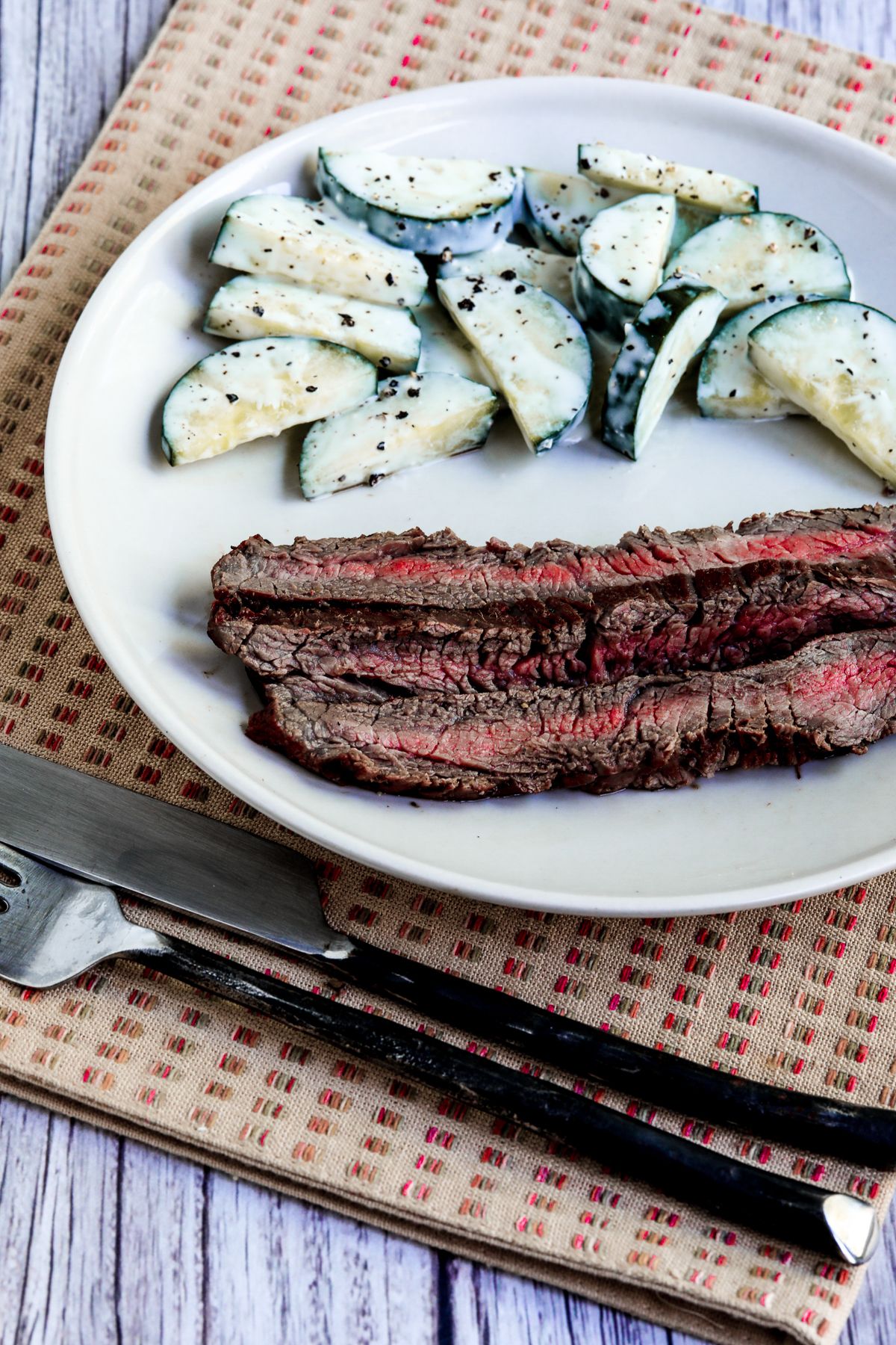 Marinated Grilled Flank Steak shown on serving plate with Cucumbers Caesar.