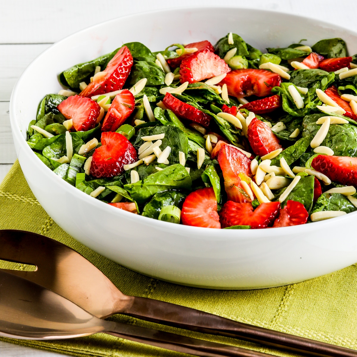 Square image of strawberry and spinach salad laid out in a serving bowl.