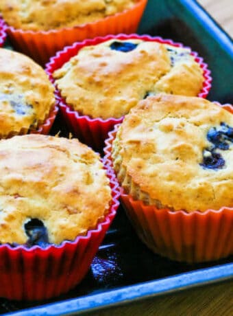 Low-Sugar Blueberry Muffins shown in muffin baking cups on baking sheet.