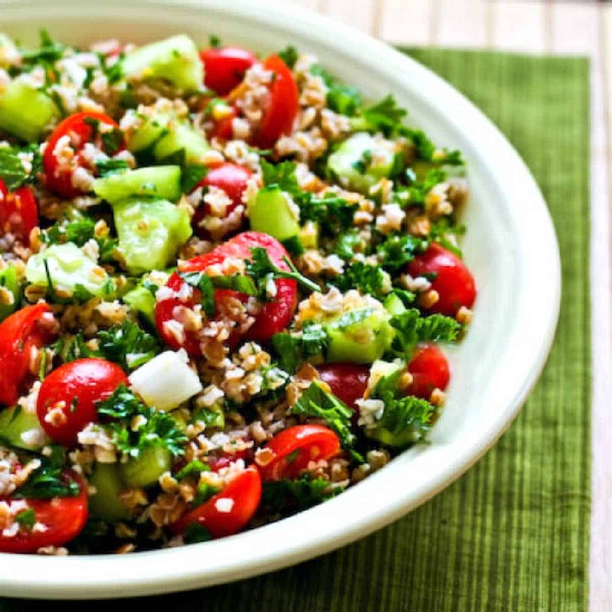 Bulgur Wheat Salad with Tomatoes, Cucumbers, Parsley, and Mint shown in serving bowl on green napkin.
