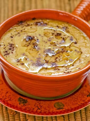 Square image of Garbanzo Bean Soup in orange bowl on decorative plate.