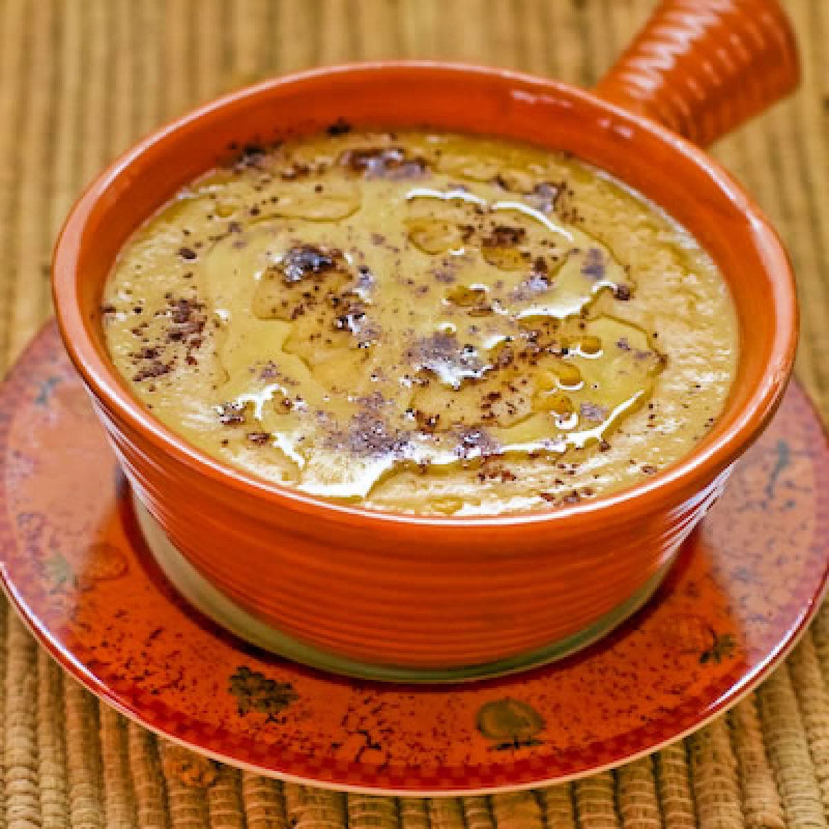 Square image of Garbanzo Bean Soup in orange bowl on decorative plate.