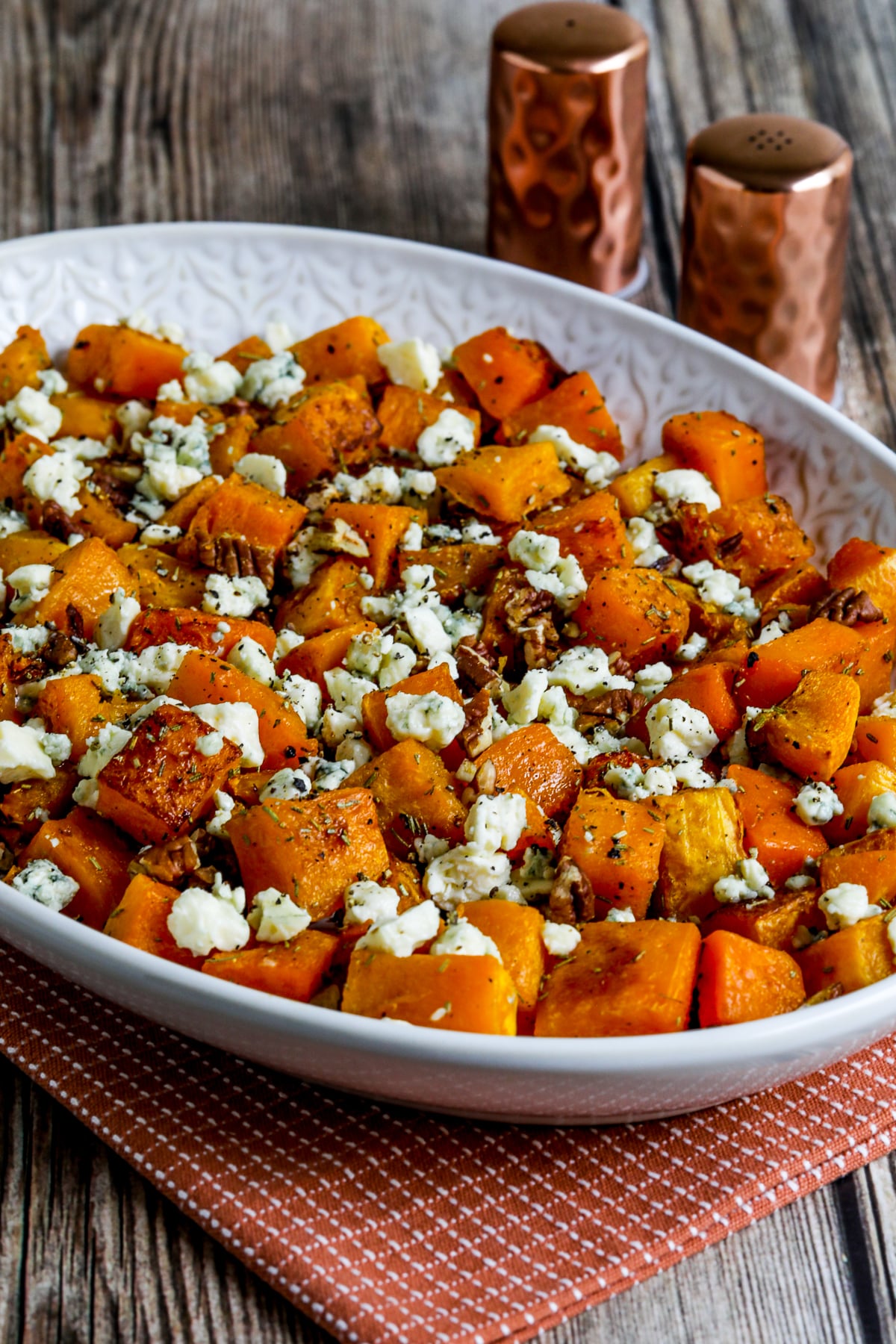 Roasted butternut squash with rosemary, pecans and gorgonzola on a serving dish with salt and pepper in the background