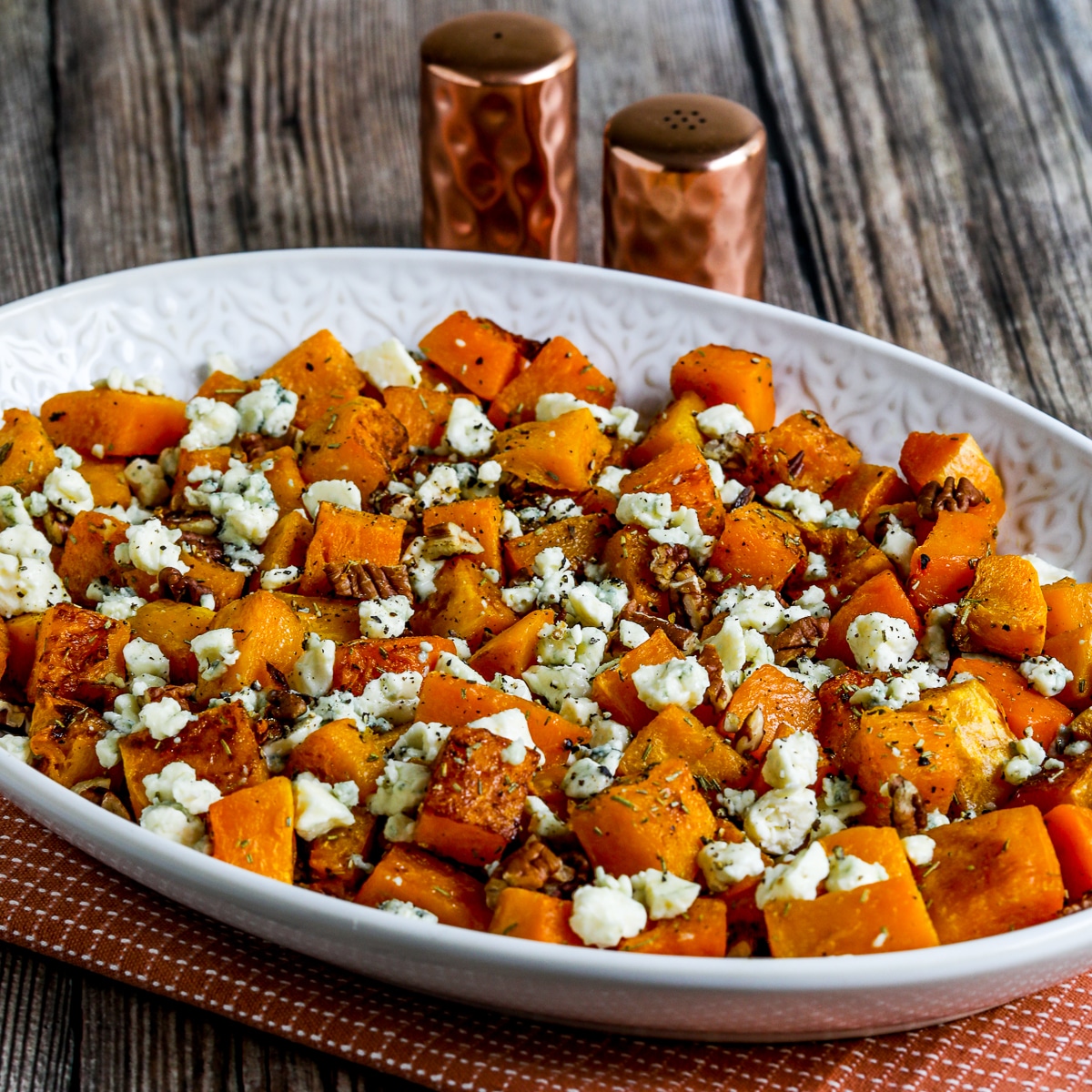 square image of Roasted Butternut Squash with Rosemary, Pecans, and Gorgonzola on serving plate with salt-pepper in background