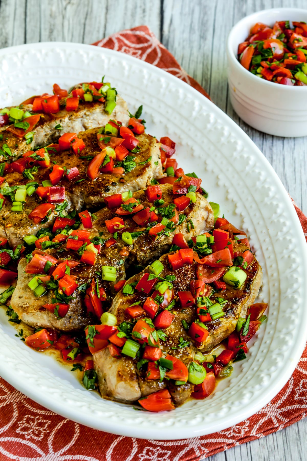 Creole Pork Chops with Tomato-Pepper Relish shown on serving plate with extra relish in bowl.