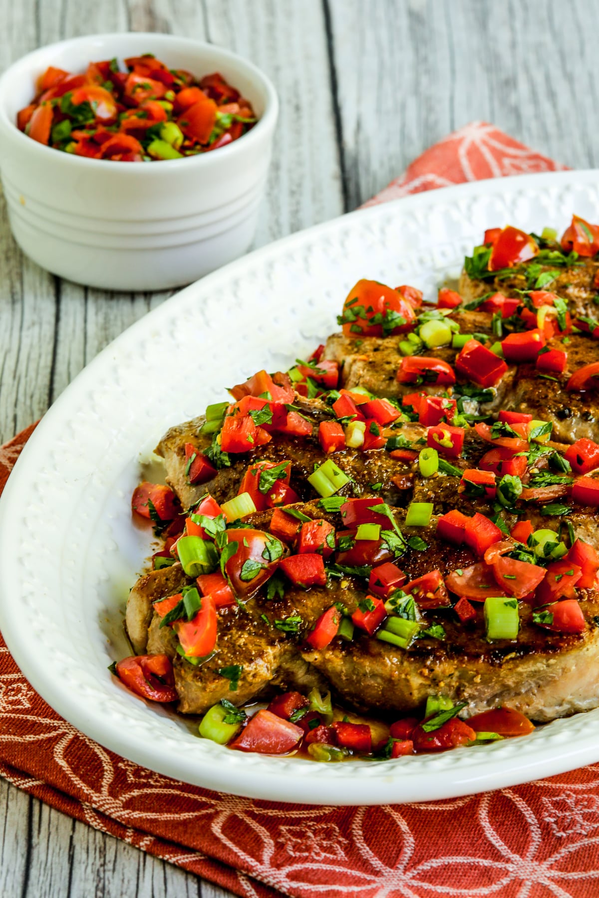 Creole pork chop with tomato pepper relish served on a plate with additional relish in a bowl.  Second image.