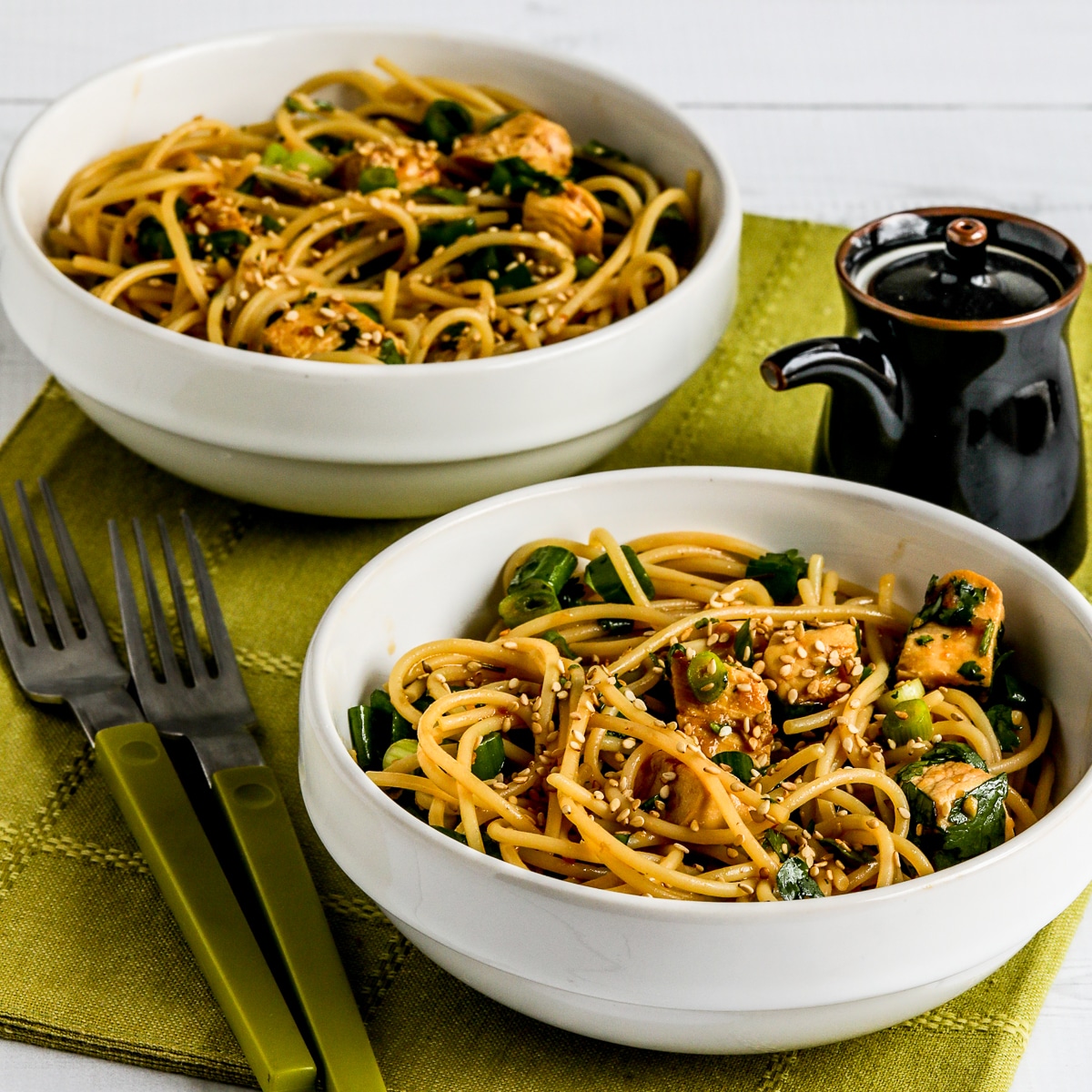 Square image of Sesame Noodles with Chicken in two serving bowls with soy sauce and green forks.
