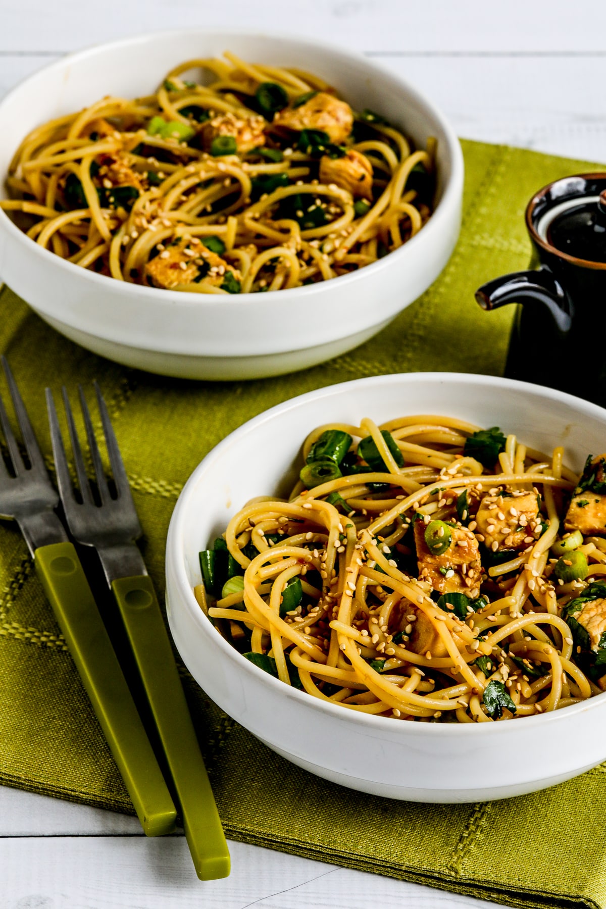 Sesame Noodles with Chicken in two serving bowls with soy sauce and green forks.