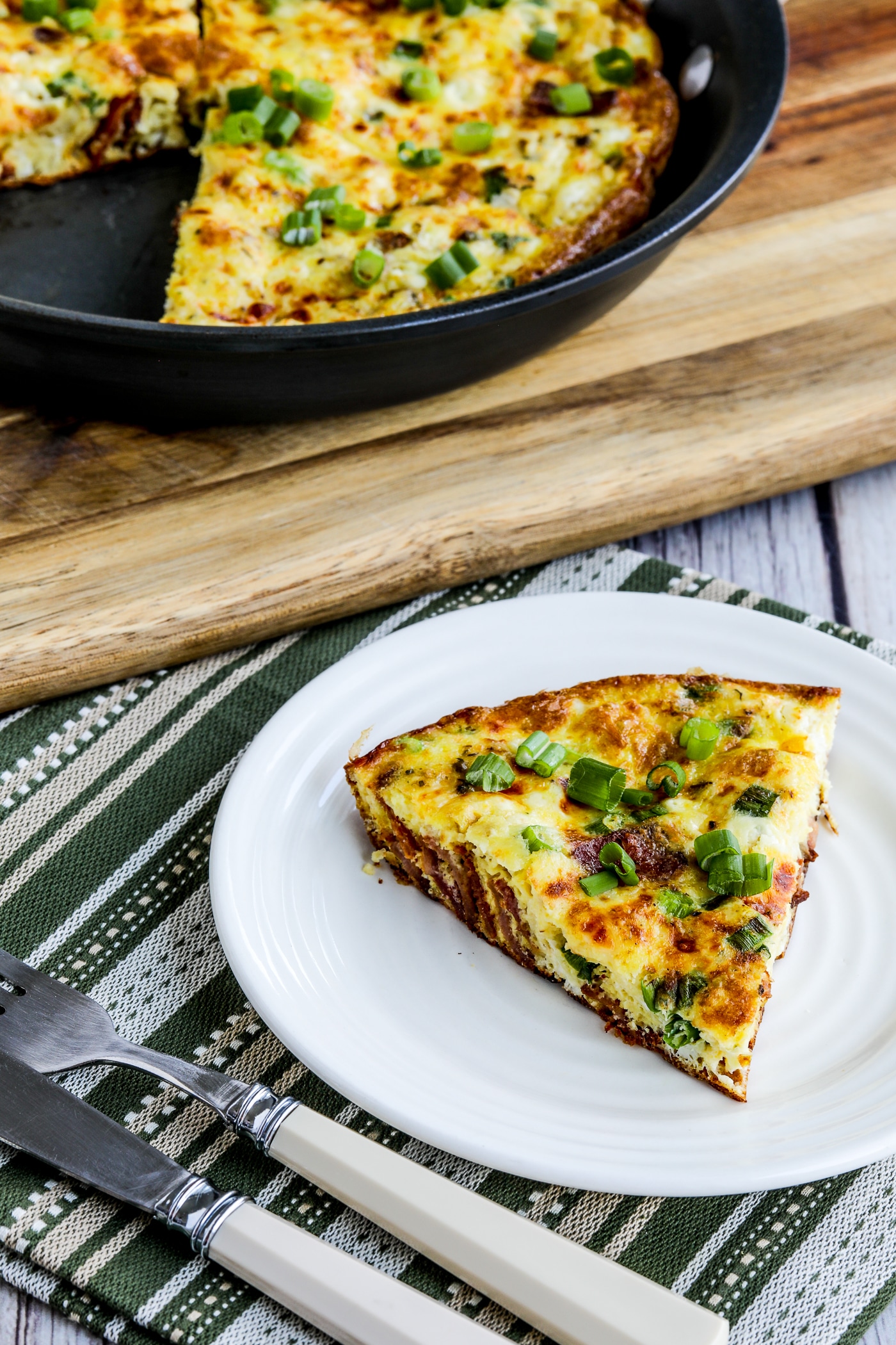 Bacon Frittata with Two Cheeses one slice on serving dish and frittata in pan in background