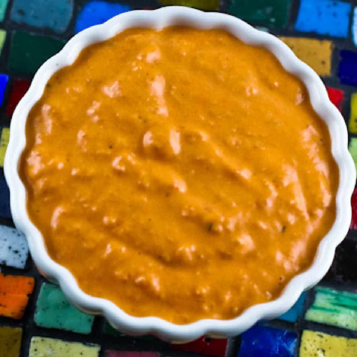 Square image of roasted red pepper sauce shown in a bowl on tiles