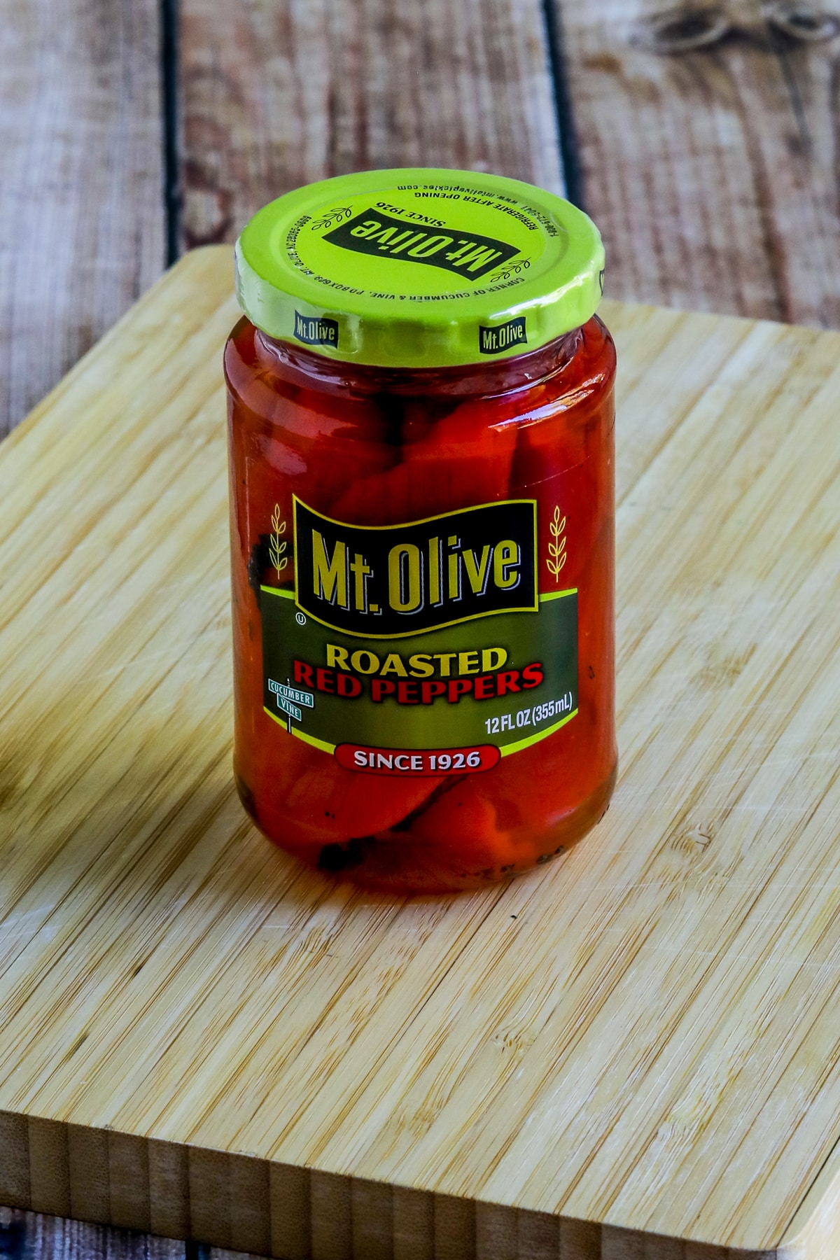 Roasted Red Peppers in a jar shown on cutting board.