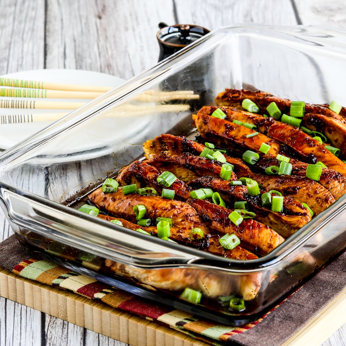 Square image of Baked Teriyaki Chicken shown in baking dish with green onion garnish.