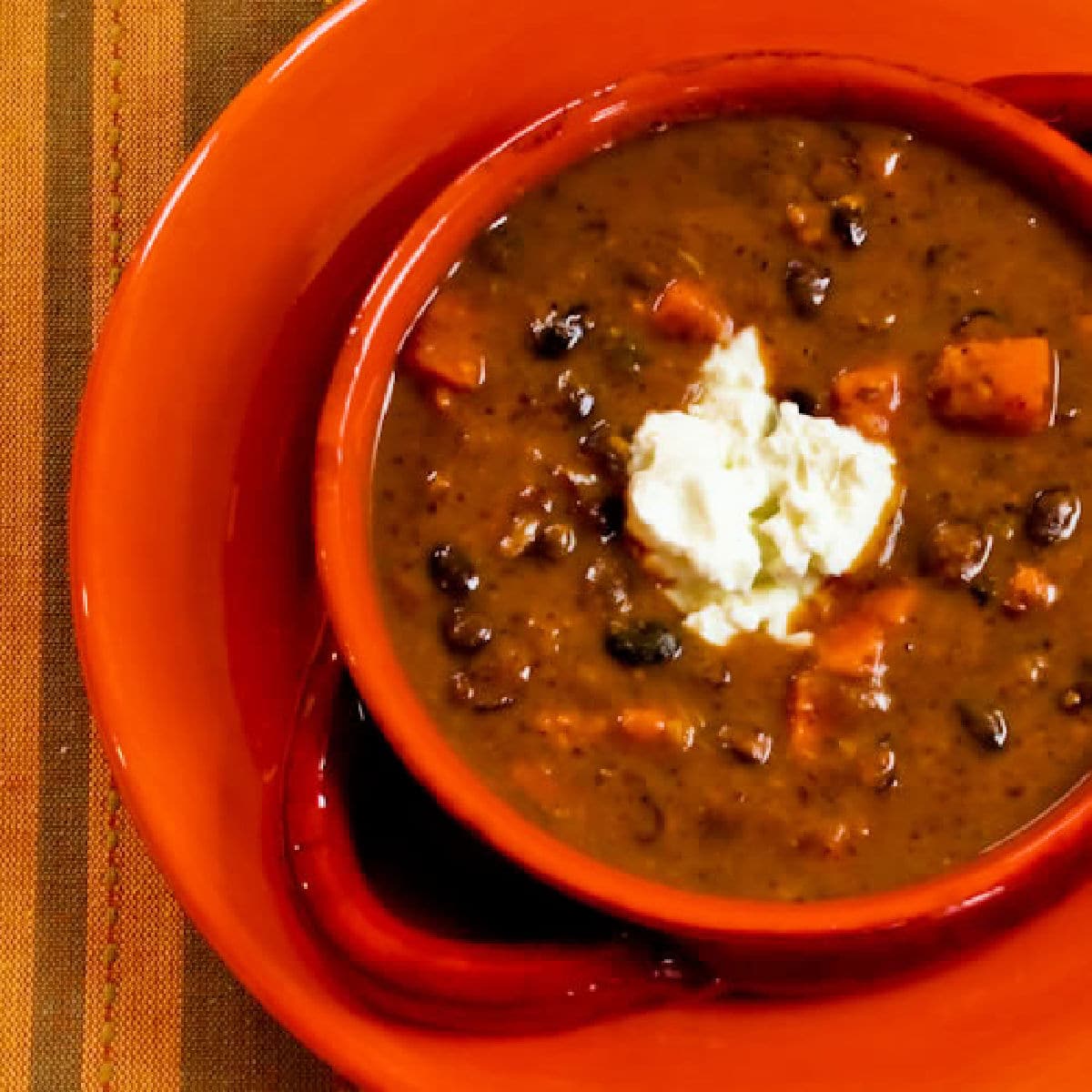 Square image for Black Bean Sweet Potato Soup in orange bowl with sour cream on top.