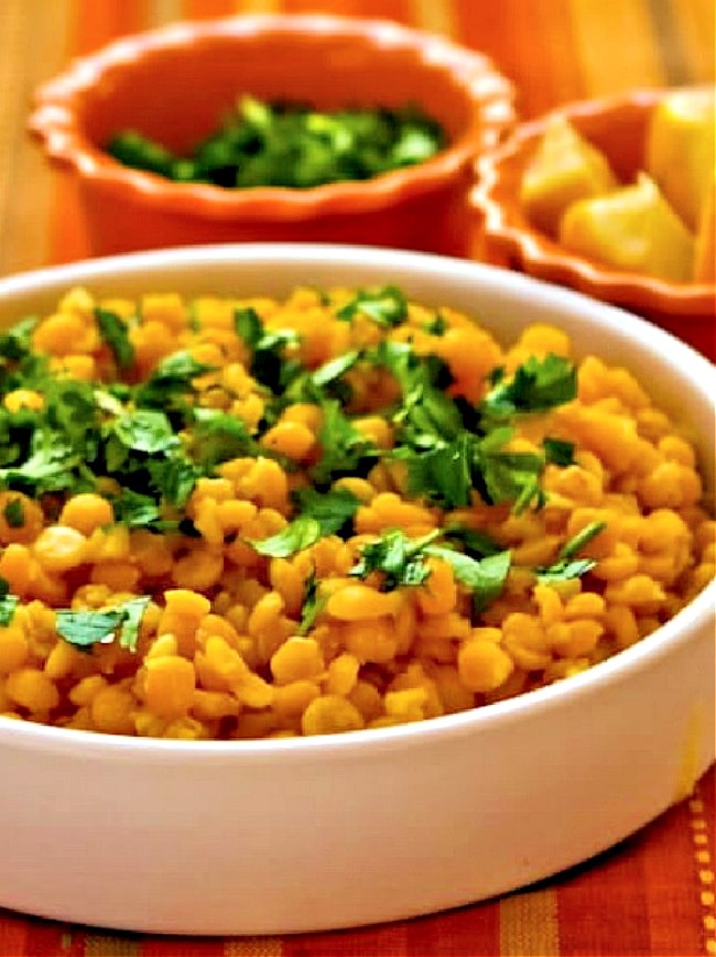 Lemony Yellow Split Pea Recipe in serving bowl with lemons and cilantro in back.