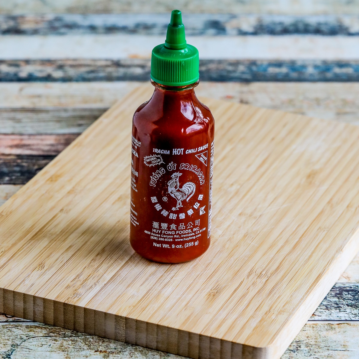 Square image of Sriracha Sauce bottle shown on cutting board.