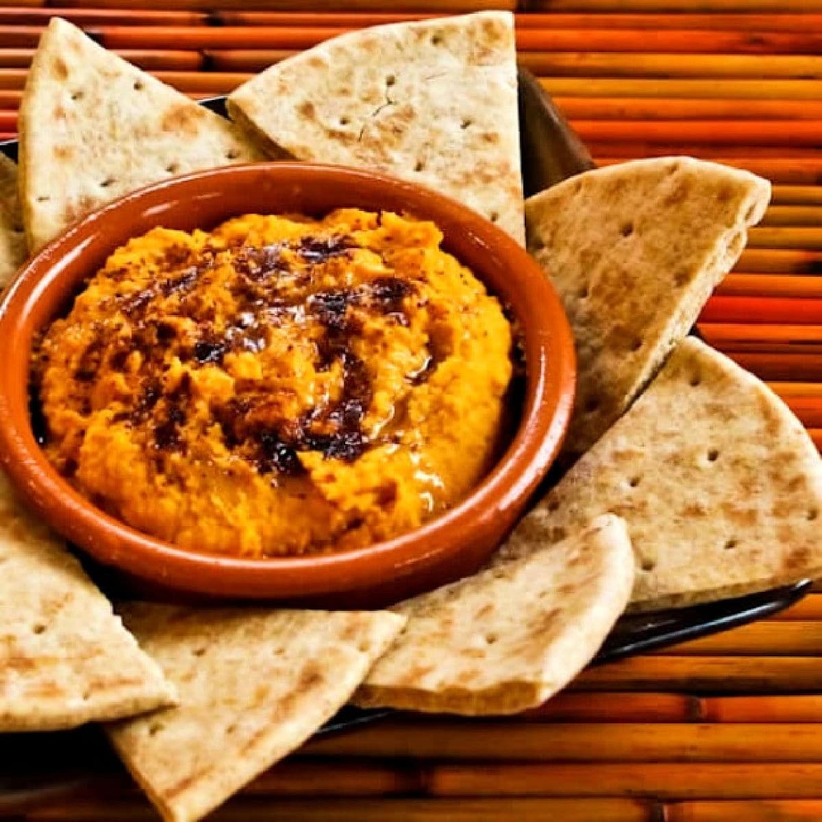 Sweet potato hummus shown in serving dish with pita bread around it.