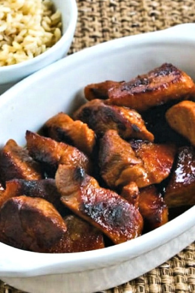 Filipino Pork Adobo shown in serving dish with rice in background.