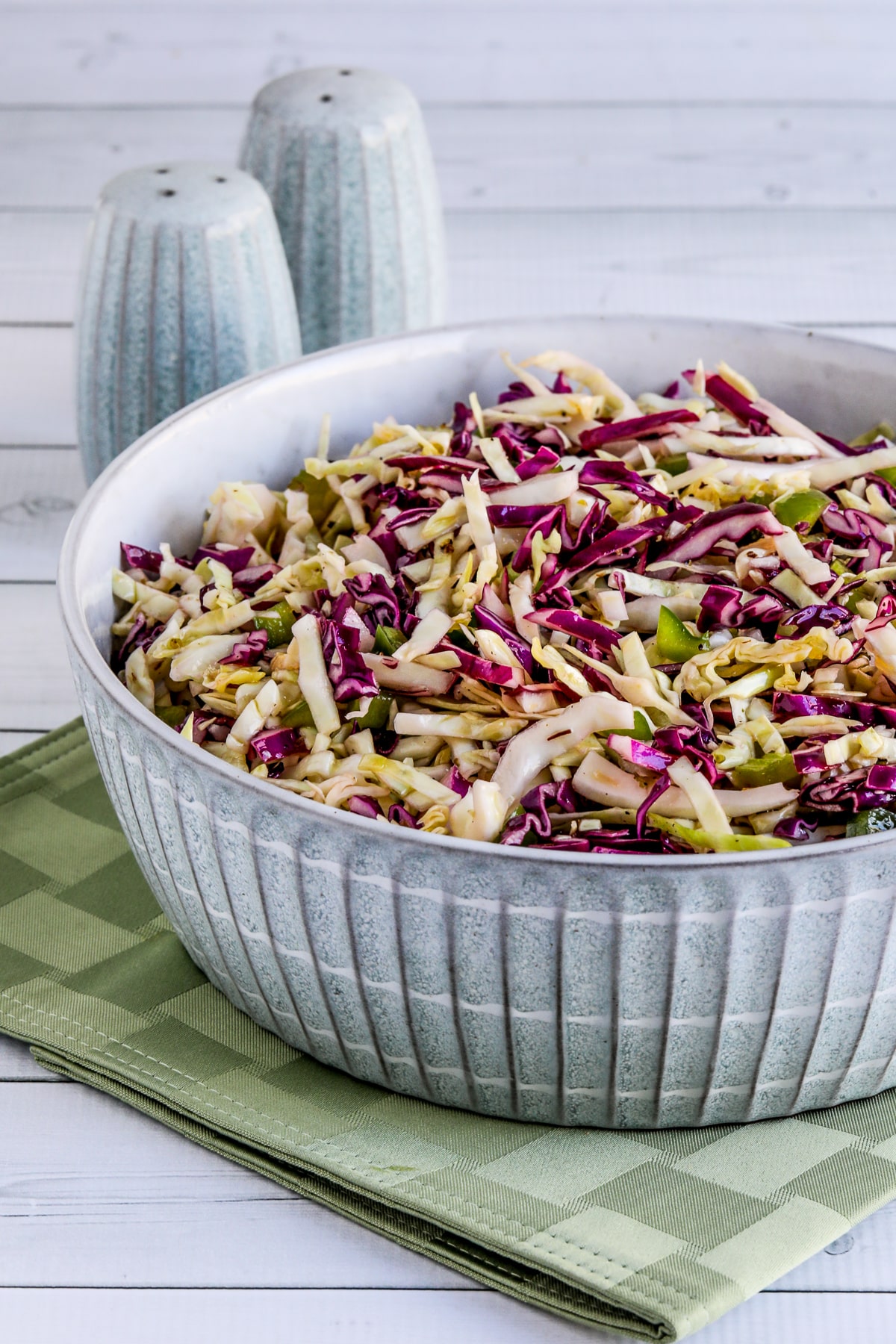 No-Mayo Vinegar Coleslaw shown in bowl on green napkin with salt and pepper in back.