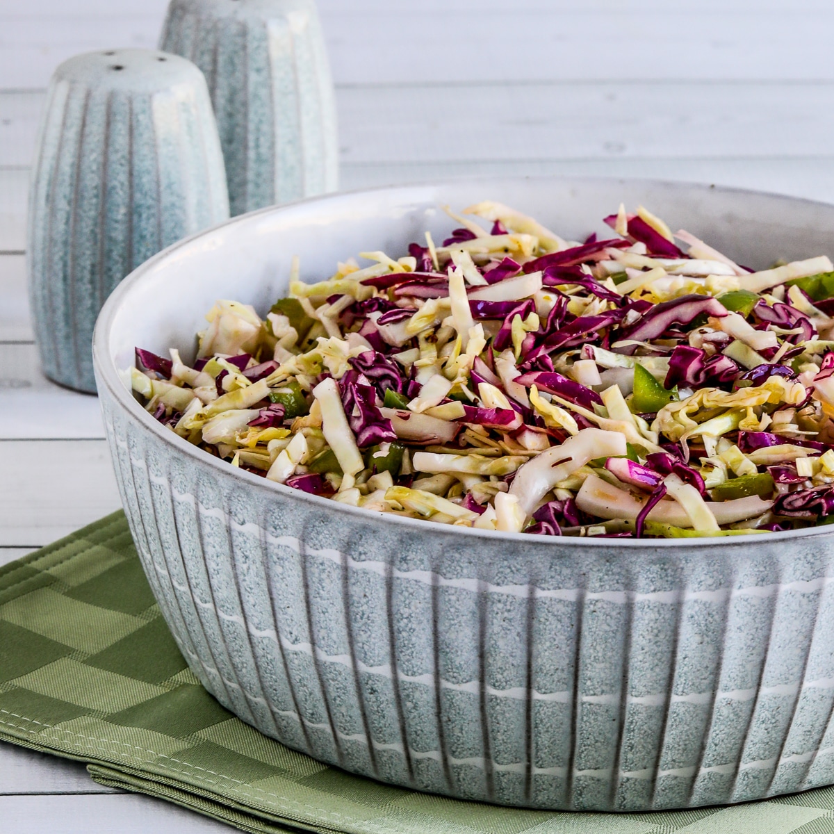 No-Mayo Vinegar Coleslaw shown in serving dish with salt and pepper in background.