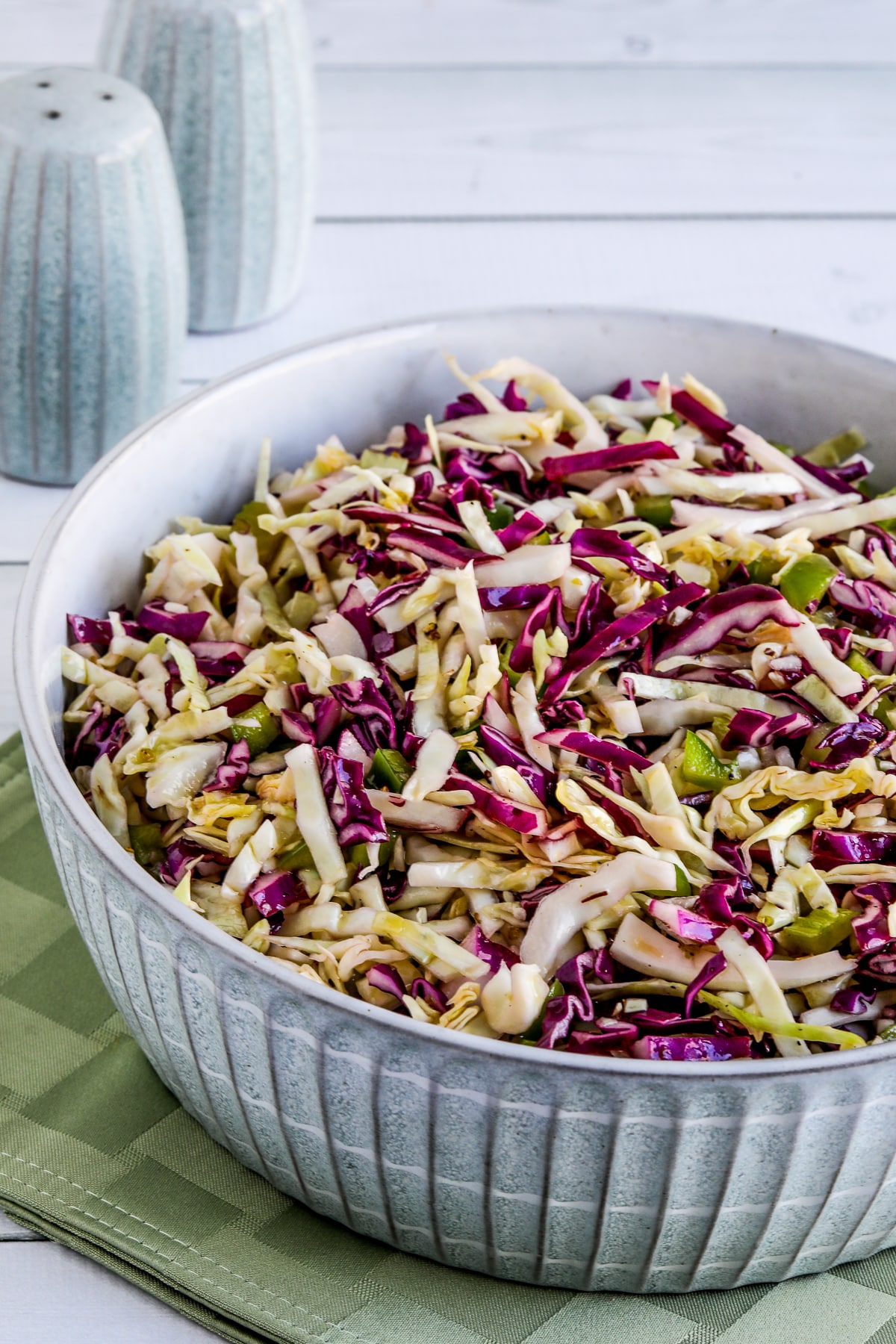 Vinegar Coleslaw shown in serving bowl with salt-pepper in background.