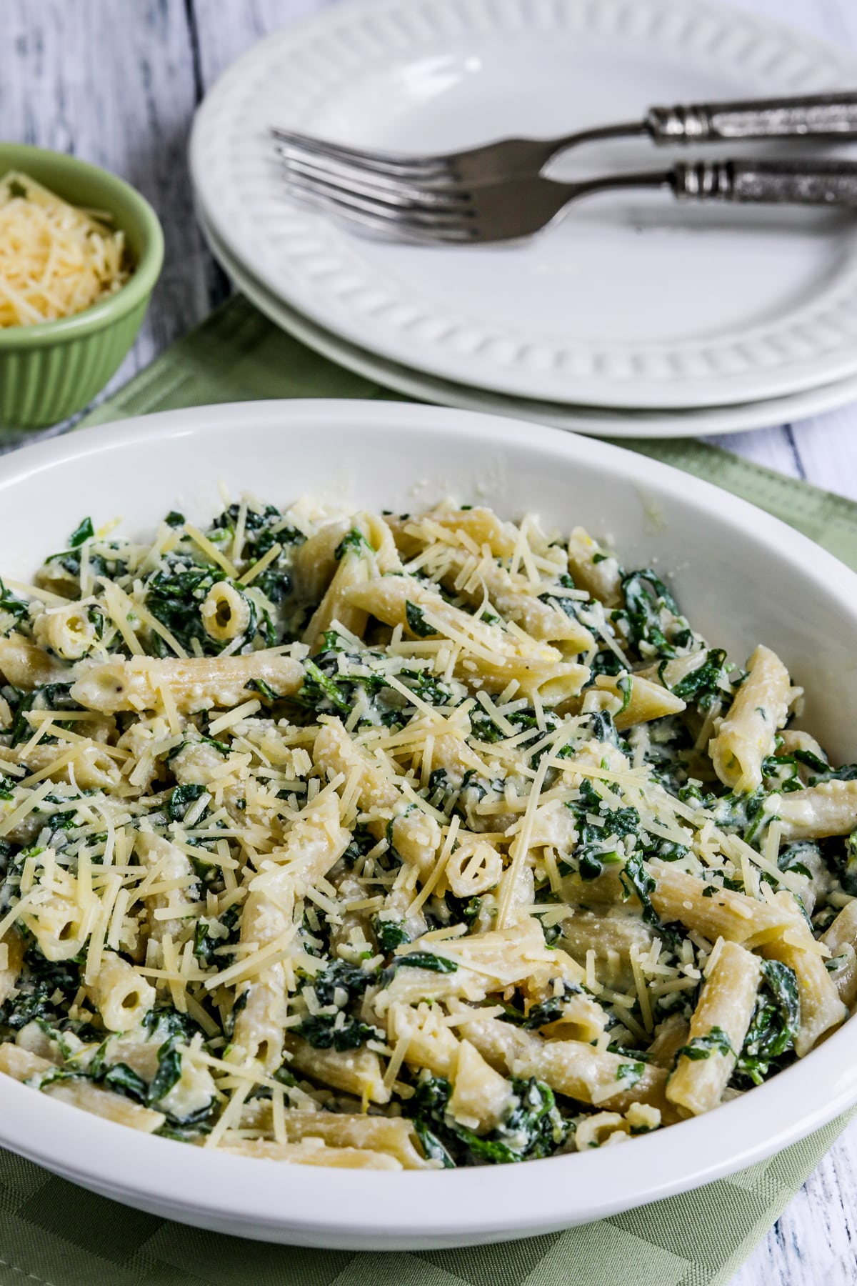 Pasta with Creamy Arugula Sauce shown in serving dish with Parmesan, plates, and forks in background