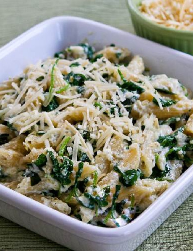 Pasta with Creamy Arugula Sauce shown in serving dish with Parmesan in background