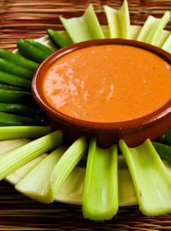Square image of Roasted Red Pepper Dip with Feta in serving bowl with celery and sugar snap peas.