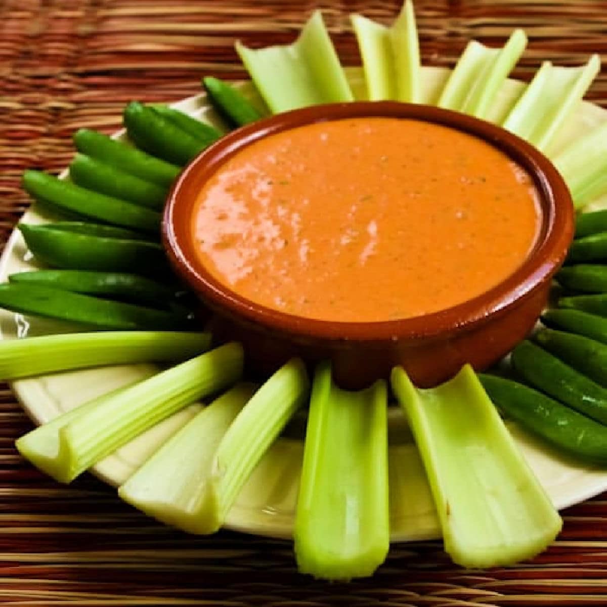Square image of Roasted Red Pepper Dip with Feta in serving bowl with celery and sugar snap peas.