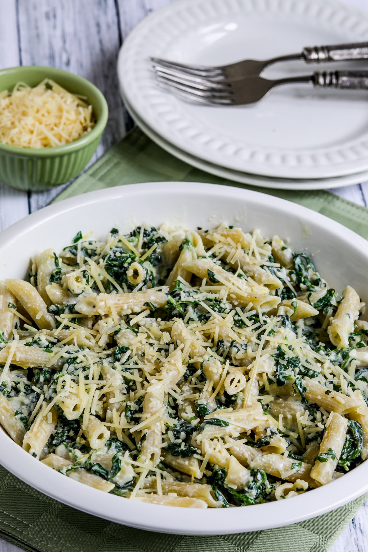 Pasta with Creamy Arugula Sauce in serving dish with plates, forks, and Parmesan.